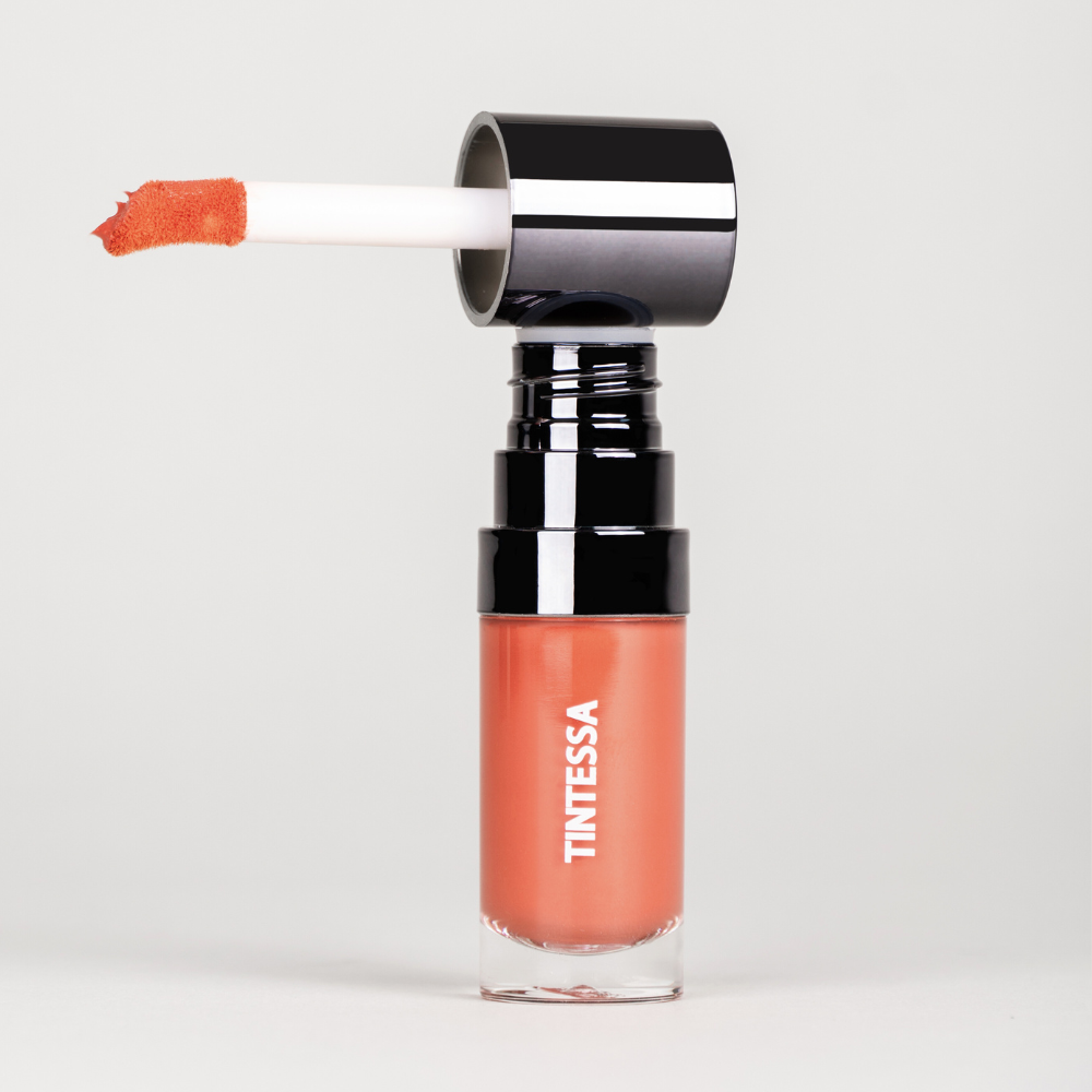 Cheek, lips and lids multi-use tint in coral rust colour with applicator on a white background