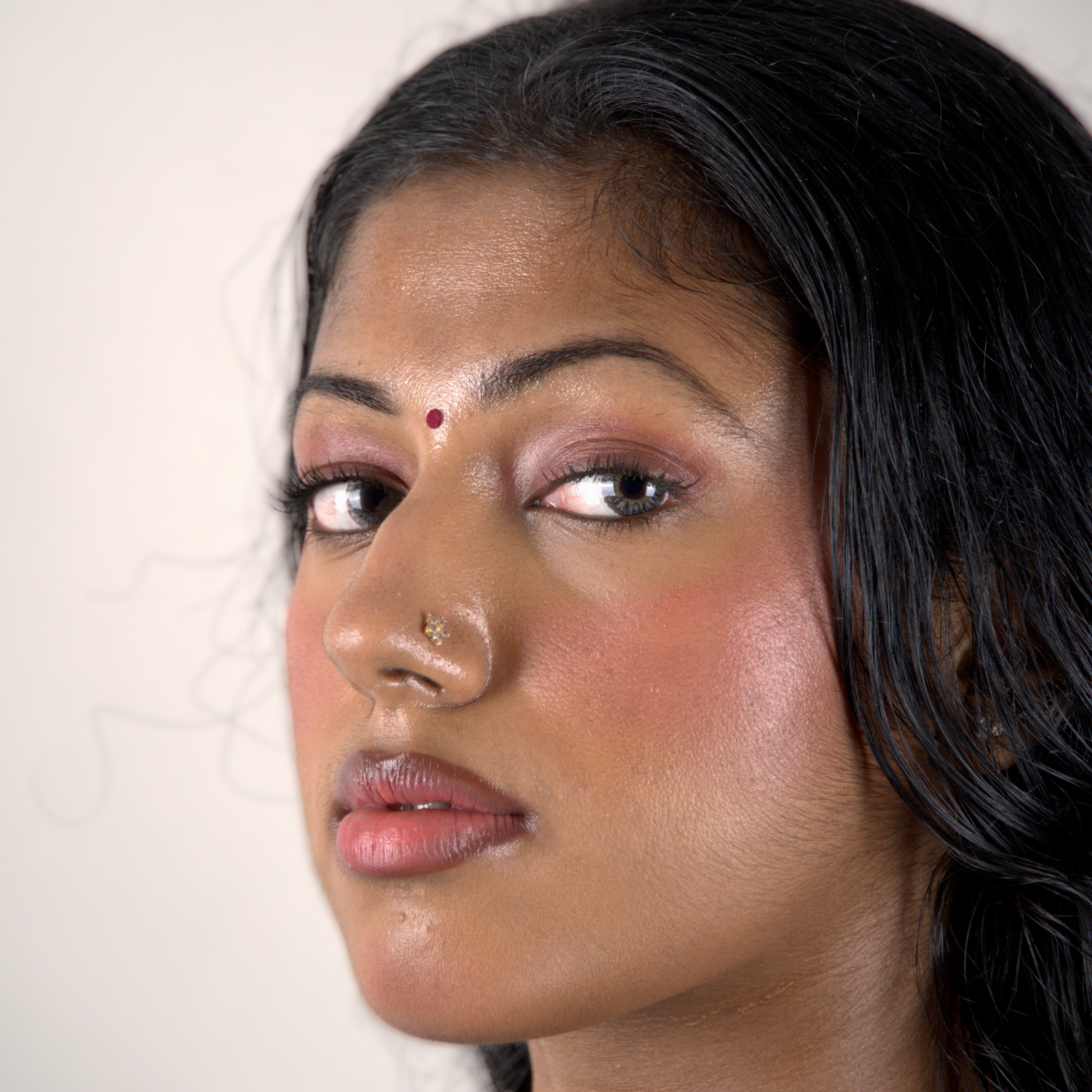 Close-up of a brown girl against a plain background wearing pink lip and cheek tint