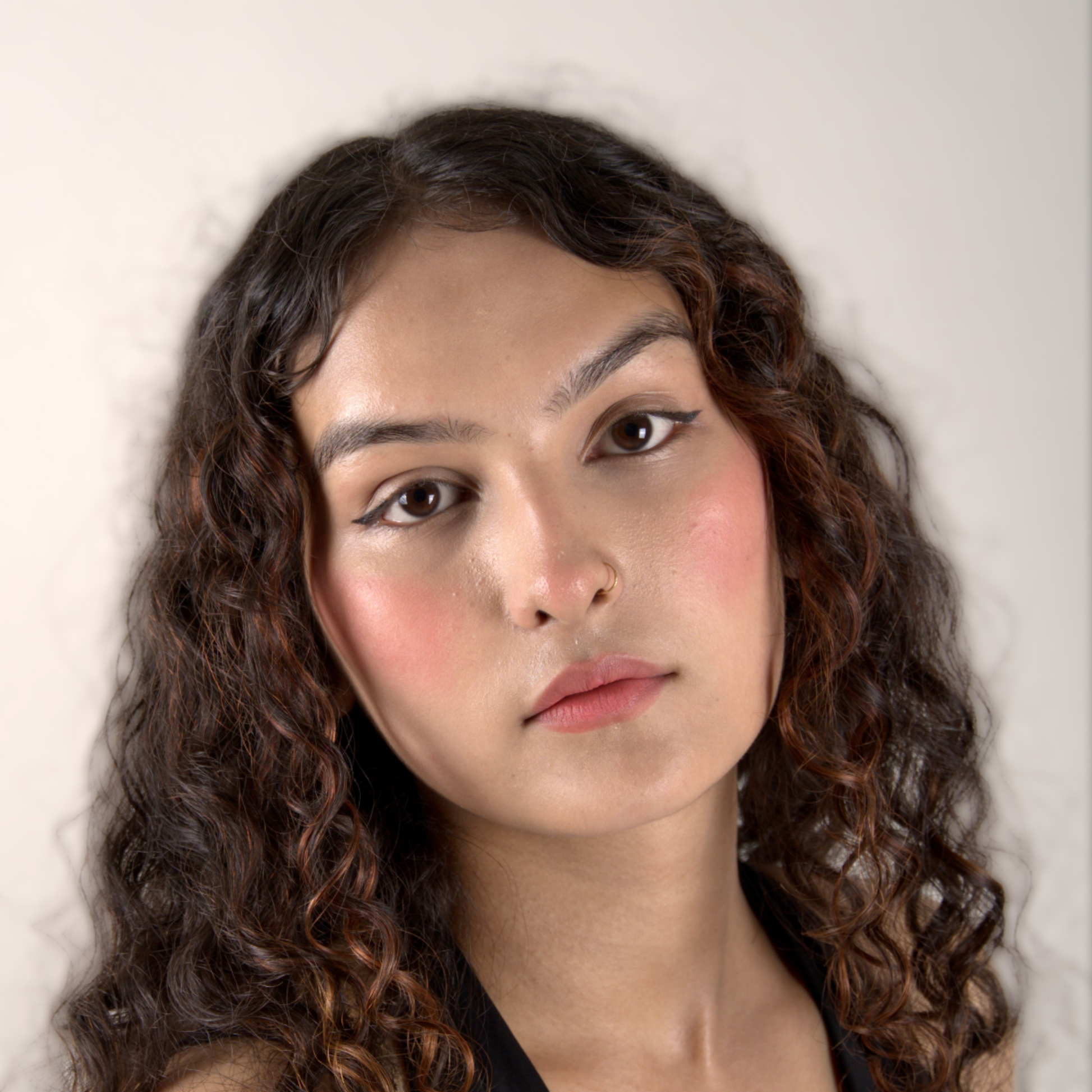Close-up of a person with curly hair against a plain background wearing pink lip and cheek tint