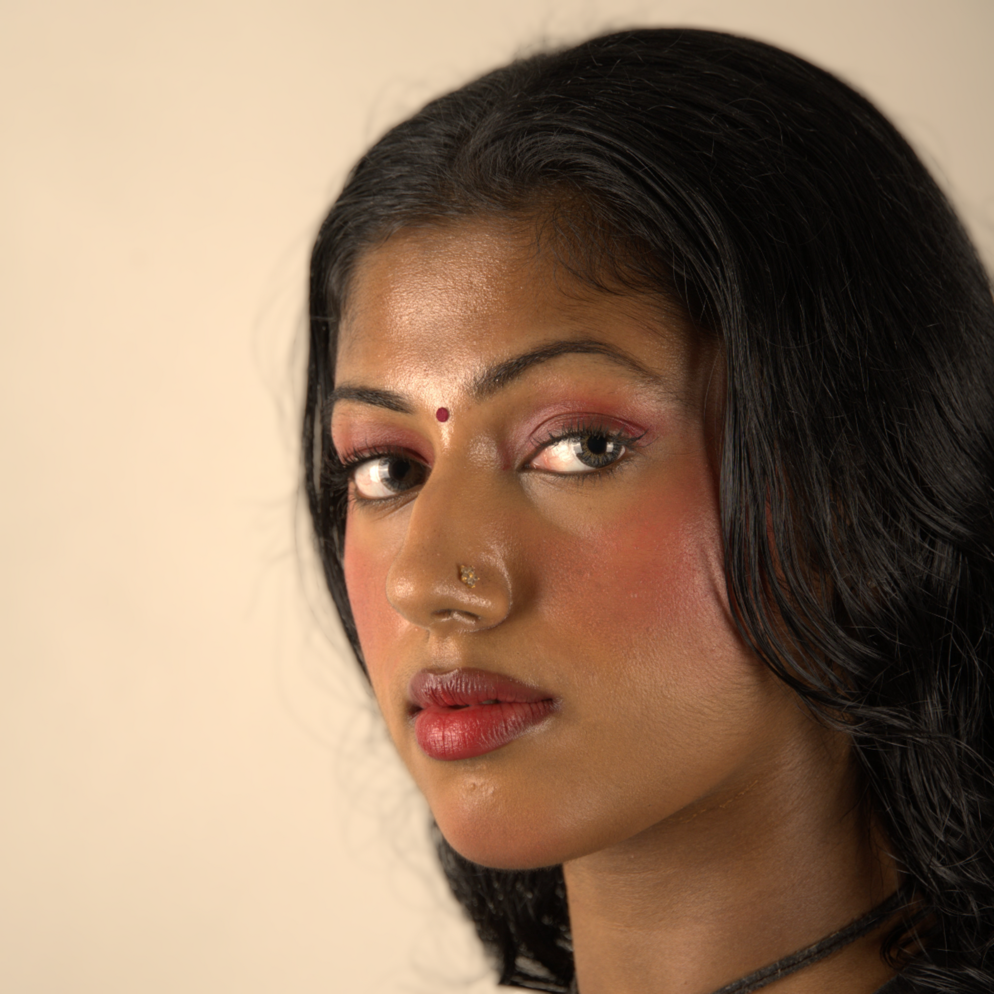 Close-up of a woman with dark hair and red lip and cheek tint against a plain background