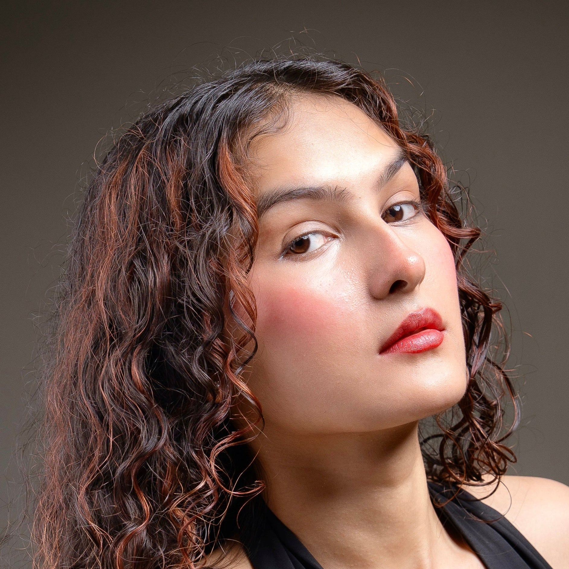 Woman with wavy hair and red lip and cheek tint against a dark background