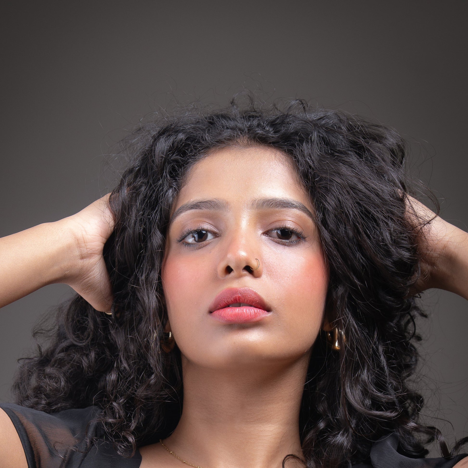 Woman with styled hair posing against a gray background wearing a sunset red lip and cheek tint