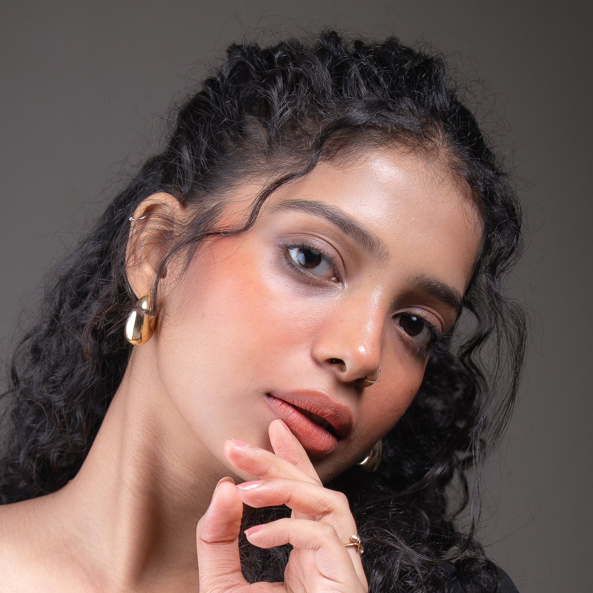 Woman with styled hair and makeup against a gray background wearing warm rust coral colur lip and cheek tint