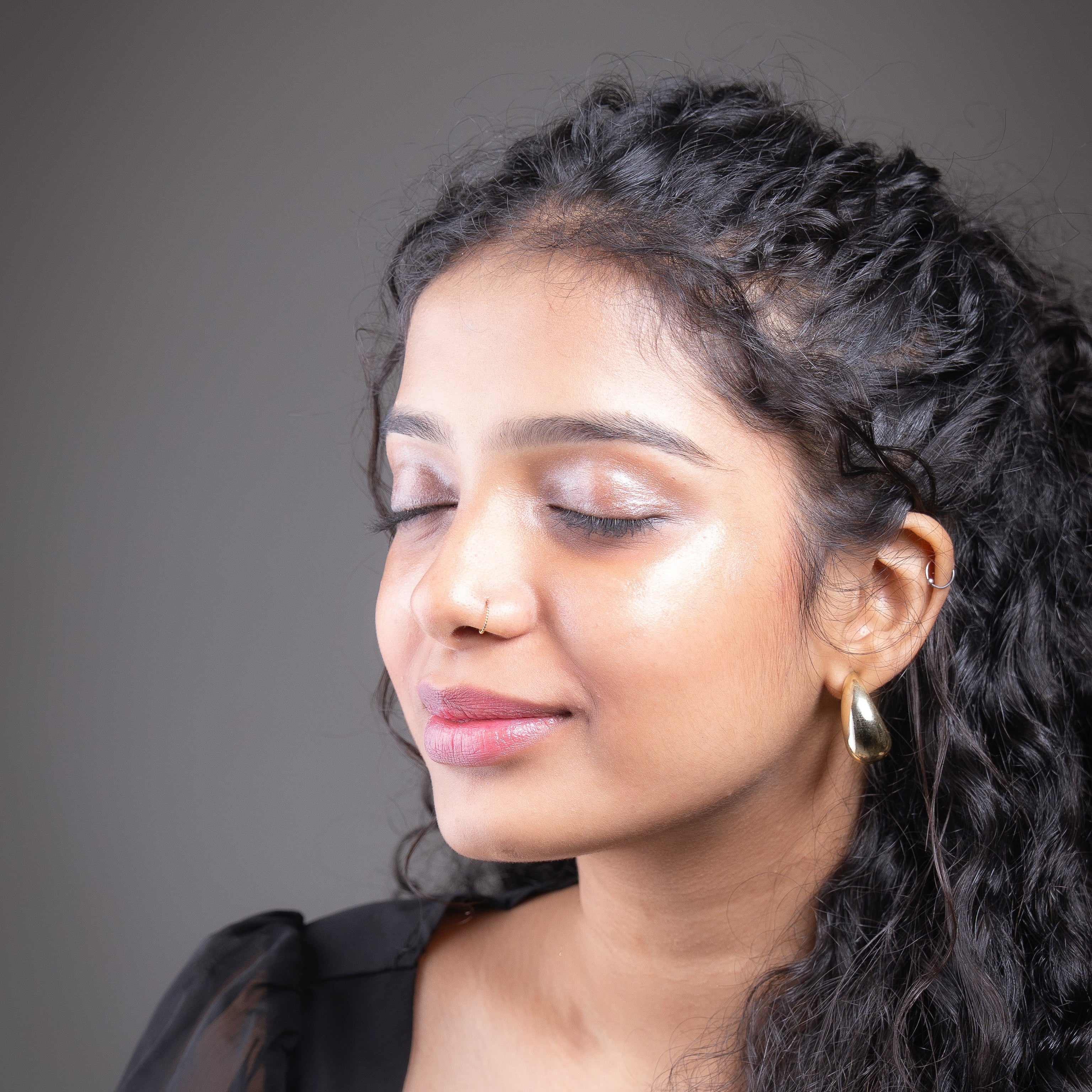 Woman wearing a black top and a champagne colour micro shimmer within glow highlighter against a dark background